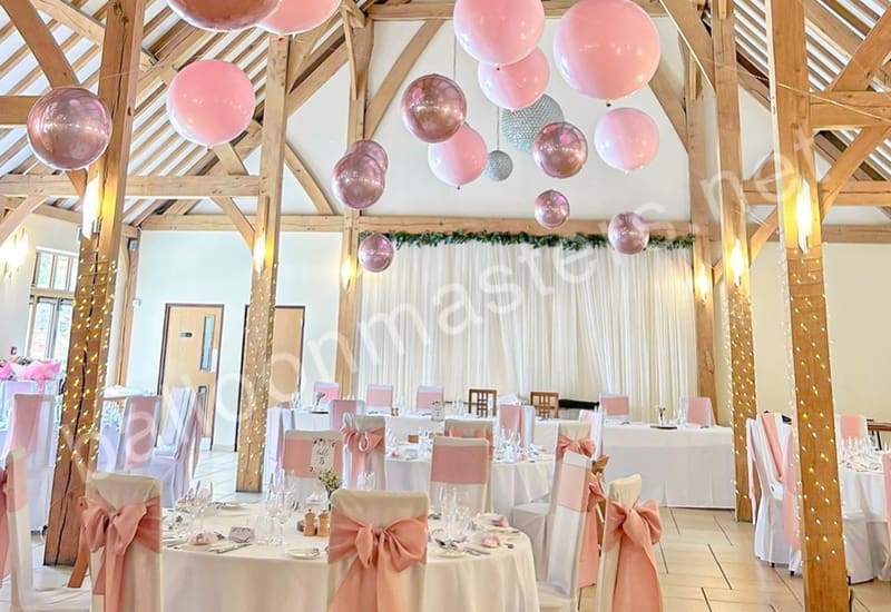 Pink and rose gold balloons strung individually from ceiling above circular tables.